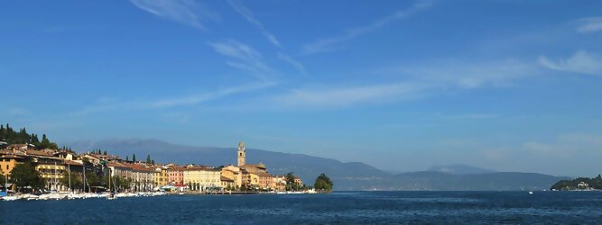 Trip Wien beliebte Urlaubsziele am Gardasee -  Mit einer Fläche von 370 km² ist der Gardasee der größte See Italiens. Es liegt am Fuße der Alpen und erstreckt sich über drei Staaten: Lombardei, Venetien und Trentino. Die maximale Tiefe des Sees beträgt 346 m, er hat eine längliche Form und sein nördliches Ende ist sehr schmal. Dort ist der See von den Bergen der Gruppo di Baldo umgeben. Du trittst aus deinem gemütlichen Hotelzimmer und es begrüßt dich die warme italienische Sonne. Du blickst auf den atemberaubenden Gardasee, der in zahlreichen Blautönen schimmert - von tiefem Dunkelblau bis zu funkelndem Türkis. Majestätische Berge umgeben dich, während die Brise sanft deine Haut streichelt und der Duft von blühenden Zitronenbäumen deine Nase kitzelt. Du schlenderst die malerischen, engen Gassen entlang, vorbei an farbenfrohen, blumengeschmückten Häusern. Vereinzelt unterbricht das fröhliche Lachen der Einheimischen die friedvolle Stille. Du fühlst dich wie in einem Traum, der nicht enden will. Jeder Schritt führt dich zu neuen Entdeckungen und Abenteuern. Du probierst die köstliche italienische Küche mit ihren frischen Zutaten und verführerischen Aromen. Die Sonne geht langsam unter und taucht den Himmel in ein leuchtendes Orange-rot - ein spektakulärer Anblick.